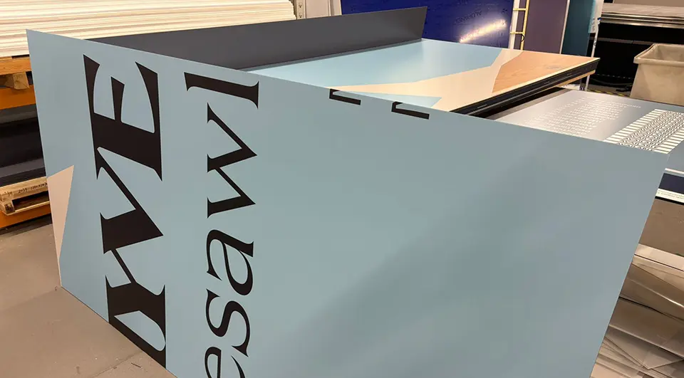 How much does Hoarding Signage Cost 2 A close-up of a large, custom-printed Dibond hoarding panel in a workshop, showing a light blue design with black serif typography.
