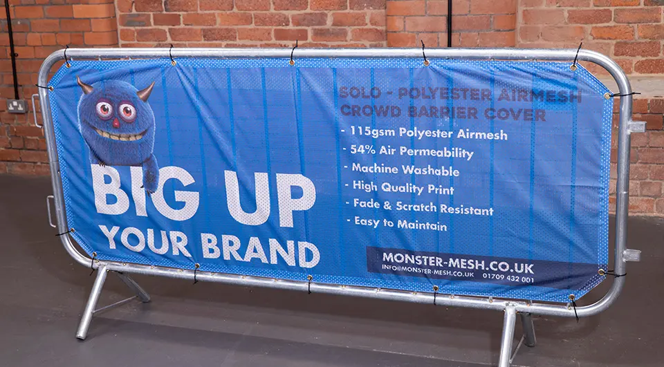 Best Crowd Barrier Covers for Your Budget 1 A blue Solo polyester airmesh crowd barrier cover with Monster-Mesh branding attached to a barrier with cable ties.