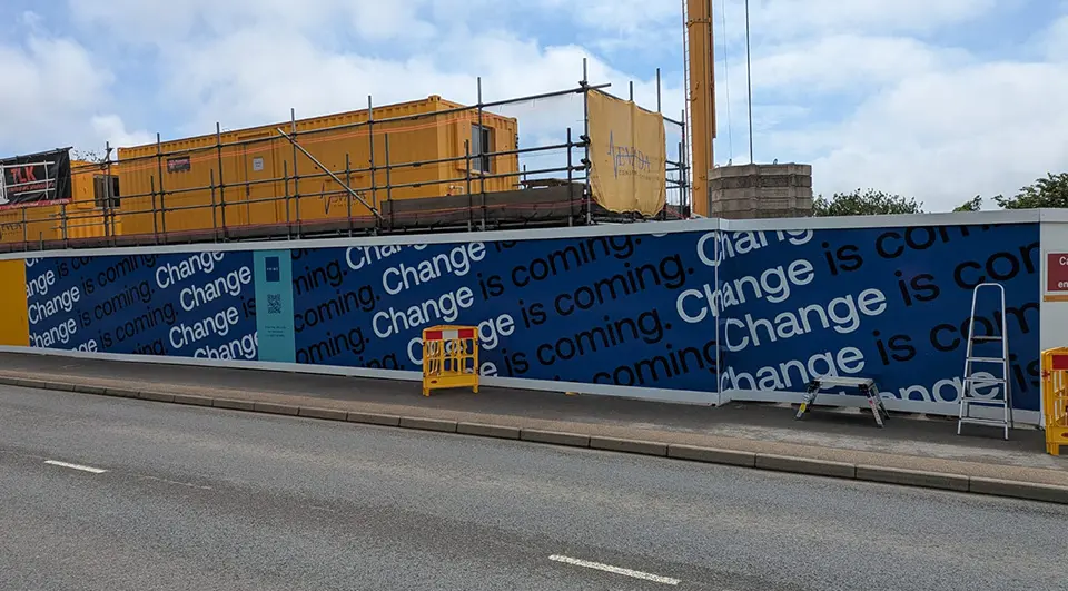 hoarding-signage-nevada-construction-installation-category-tile Installed blue and white 'Change is coming' branded hoarding signage featuring integrated QR codes on-site in Truro.