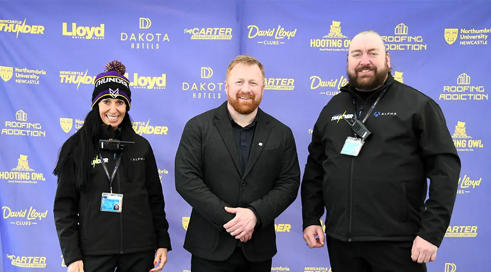 Custom Banners for Newcastle Thunder Rugby League 4 Three people pose for a photo in front of a large, custom-printed purple media wall banner filled with yellow sponsor logos.