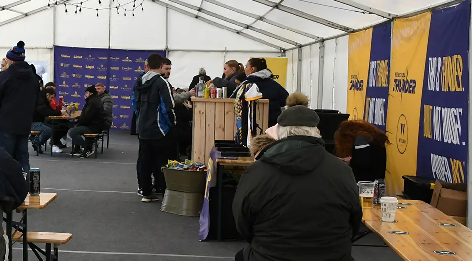 Custom Banners for Newcastle Thunder Rugby League 2 A wide-angle view inside a large match-day marquee tent during a Newcastle Thunder event. Benches and tables are set up for fans, with custom yellow and blue branded banners running along the entire right wall.